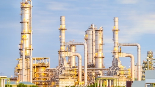 Petrochemical refinery with multiple distillation columns lit in golden tones against a clear evening sky