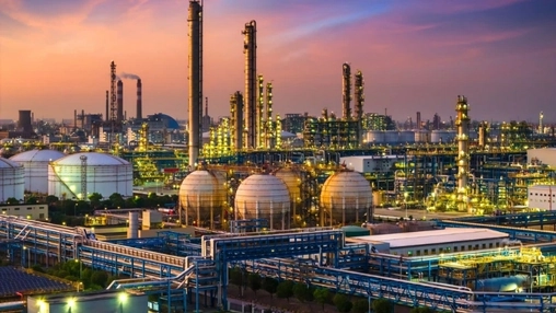 Petrochemical refinery with spherical tanks and distillation towers glowing against a purple-orange dusk sky