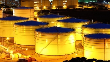 Large industrial storage tanks with blue roofs glowing amber under floodlights at a facility at night