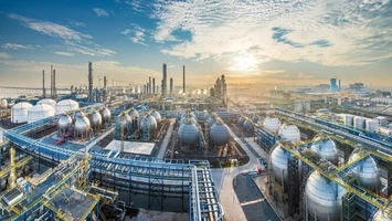 Aerial view of an integrated petrochemical complex with spherical tanks, towers, and blue piping at sunrise
