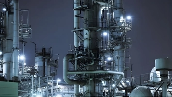 Night-time view of a petrochemical plant with lit distillation columns and pipe networks in cool blue light