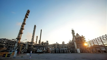 Low-angle view of a petrochemical plant at sunrise with processing columns and pipework against a blue sky